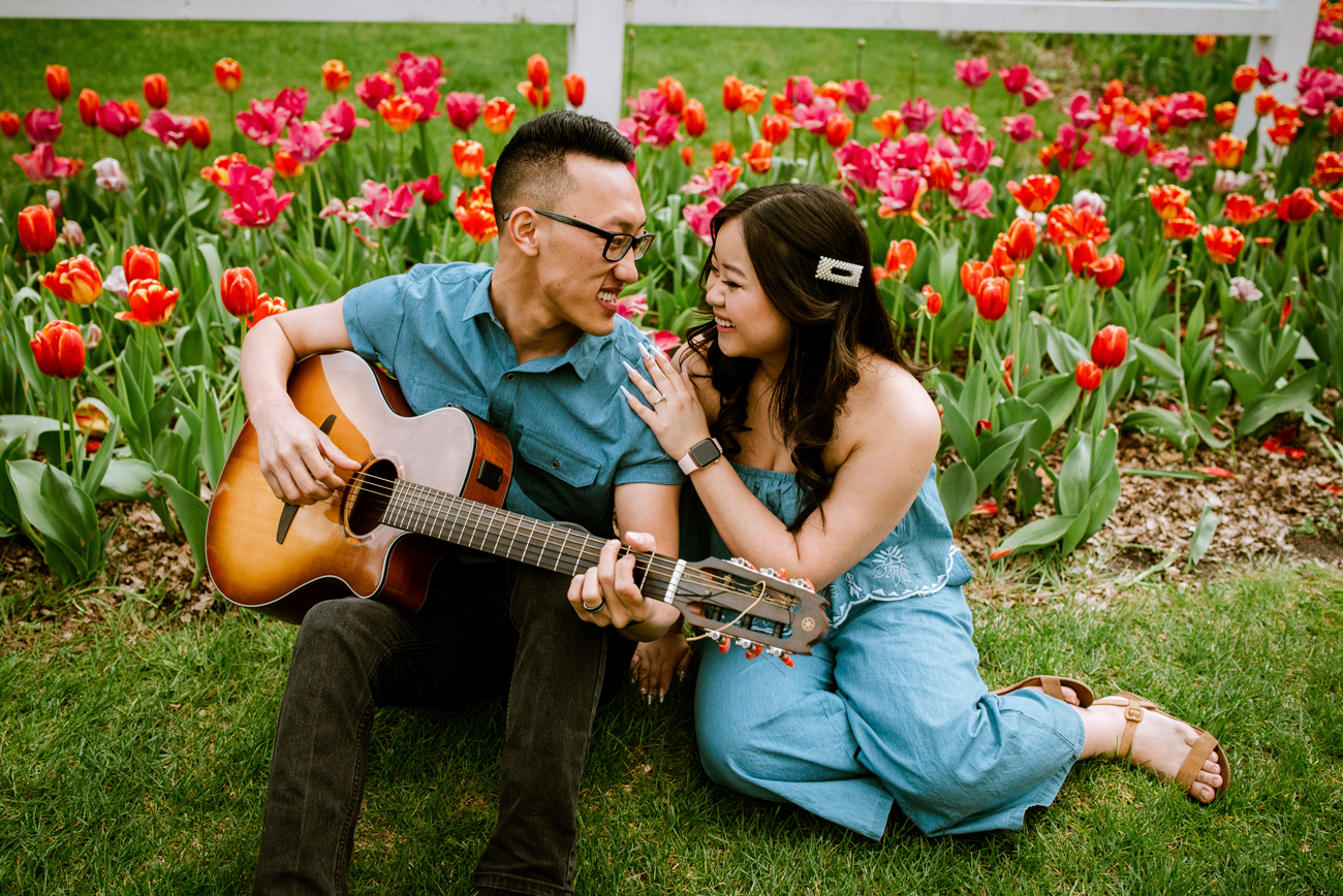 engagement photo of couple playing guitar with tulips behind them
