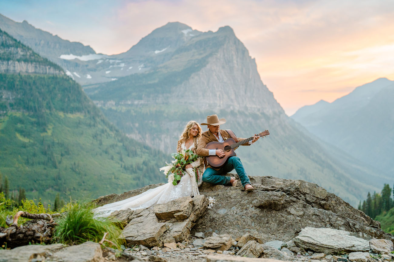 Couple sitting on a rock while playing guitar in Glacier National Park with mountains in the background