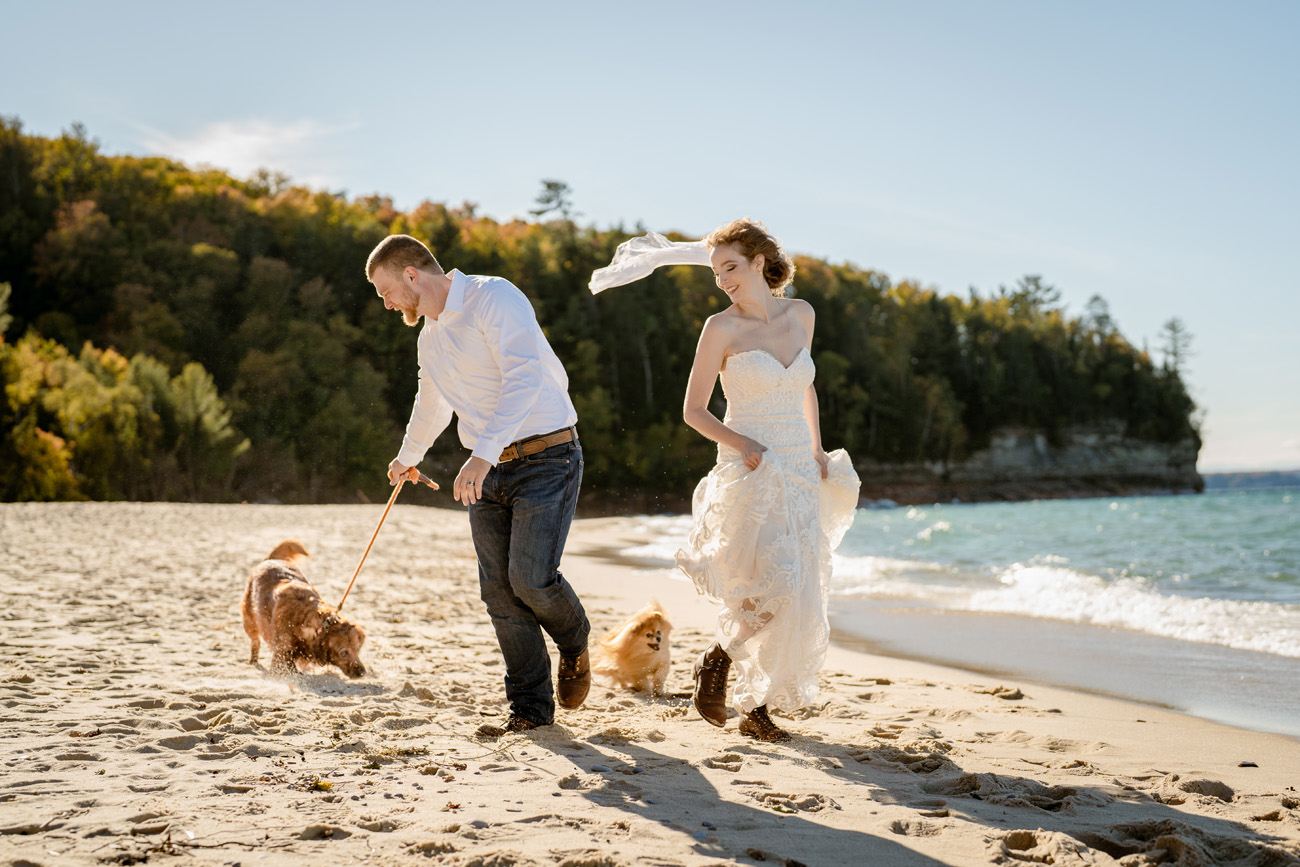couple running in wedding clothes with their dogs at a beach in the Upper Peninsula of Michigan