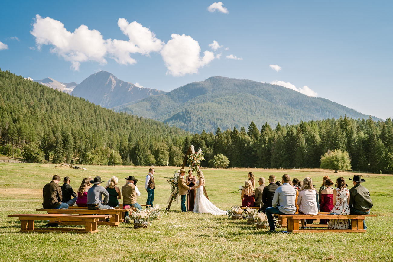 Wedding ceremony in a large field with mountains and pine trees in the background